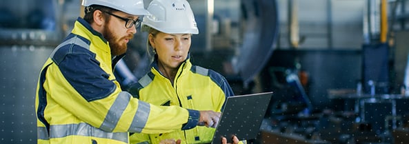 2 HVAC professional in high-visibility clothing and hardhat looking at a laptop