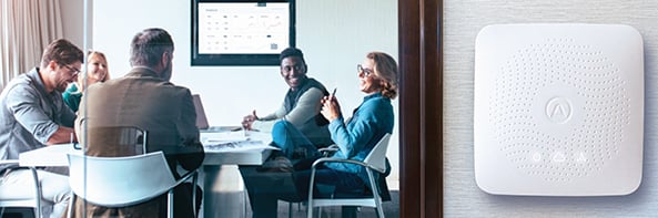 People in a meeting room with an Airthings IAQ monitor mounted on the wall