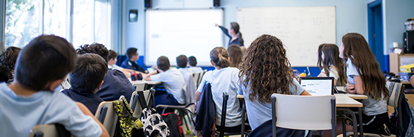 Children in a school classroom paying attention to their teacher who is presenting on an interactive whiteboard